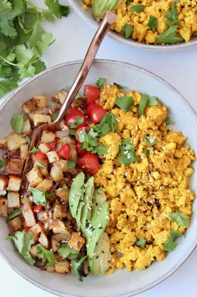 A vegan burrito bowl with tofu scramble, roasted potatoes, and fanned avocado slices